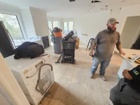 Room under renovation with construction tools, an appliance, and two workers in casual work clothes.