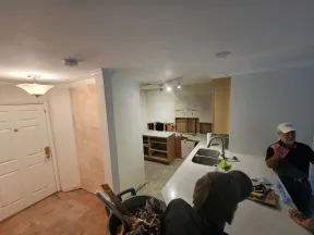 Interior view of a kitchen undergoing renovation with exposed cabinetry, a white countertop, and two men discussing work.