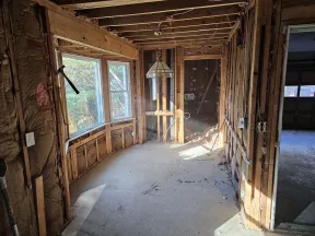 Room stripped to wooden studs and insulation with exposed ceiling and concrete floor during renovation.