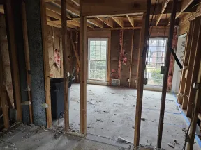 Room under renovation with exposed wooden framing, insulation, and large windows showing an outside view.