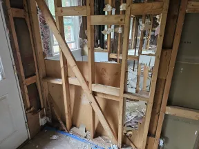 Exposed wooden wall studs and debris inside a partially demolished room under renovation near a door and window.