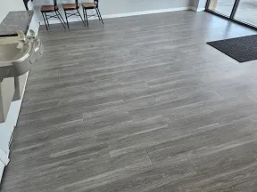 Spacious room with light gray wood-look tile flooring, water fountains, chairs, and large windows with floor mat.