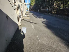 Empty outdoor alley with asphalt pavement, shadows, white buckets, and a forest background under a clear sky.