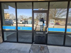 Glass storefront door of Carepoint with business hours and parking lot visible outside, located at 601A.