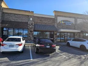 Front view of Carepoint Pharmacy with three cars parked outside in a strip mall on a sunny day.
