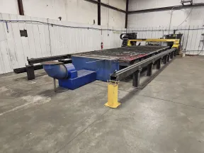 Large industrial CNC plasma cutting machine inside a spacious workshop with concrete floor and white walls.