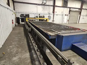Large industrial CNC plasma cutting machine inside a spacious factory with concrete floor and white walls.