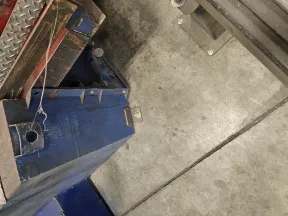 Top-down view of a blue metal industrial machine on a concrete floor in a workshop.