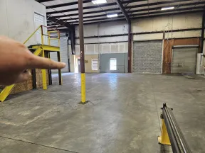 Hand pointing inside a spacious empty industrial warehouse with concrete floor and metal beams.