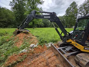 John Deere excavator moving a pile of soil on a green field under cloudy sky
