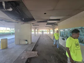 Workers in neon shirts inspecting a covered parking structure with damaged ceiling and debris scattered around.