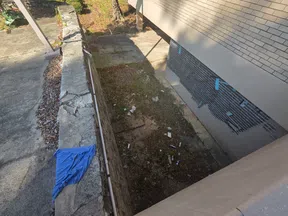 Outdoor area with cracked concrete wall, scattered trash, blue cloth, and building shadow on the ground below.