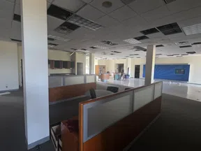 Partially renovated empty office space with cubicles, missing ceiling tiles, and workers in the background.