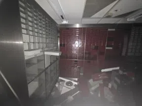 Dimly lit room with overturned red and white cabinets, debris scattered on floor, and empty shelving units.
