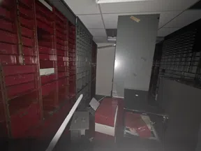 Dimly lit storage room with broken and overturned red and gray metal cabinets and shelves.