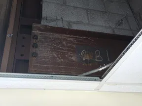 Exposed rusty steel beam with bolts above a ceiling tile in an indoor industrial setting.