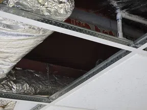 Exposed HVAC ductwork and suspended metal ceiling grid with acoustic ceiling tiles in an industrial building.