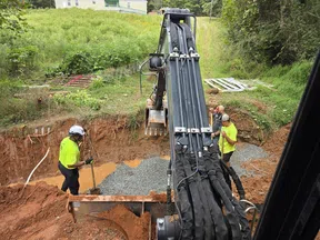 Construction workers in neon shirts operating excavator and preparing foundation with gravel in a dirt trench