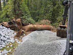 Construction site in forest with crushed stone piles, broken corrugated metal pipe, and excavator bucket.