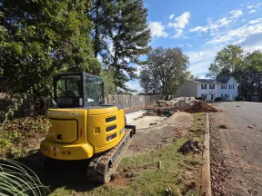 Yellow demolition excavator at a residential construction site with debris and a house in the background.