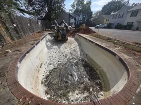 Empty residential pool under renovation with construction machinery and dirt piles surrounding it.