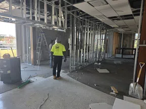 Construction workers inside a partially framed building with metal studs and exposed ceiling panels during renovation.