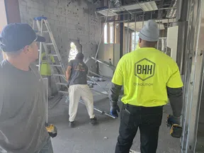 Construction workers in BHH Demolition shirts working on interior building demolition with tools and debris.