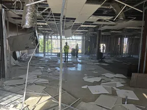 Interior of a demolished building with ceiling tiles scattered and workers in safety vests inside under construction.