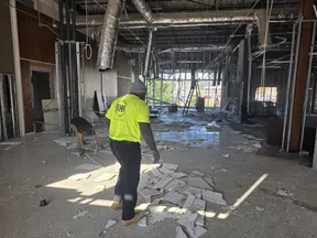 Workers in bright safety gear remove broken ceiling tiles during demolition inside a large commercial building.