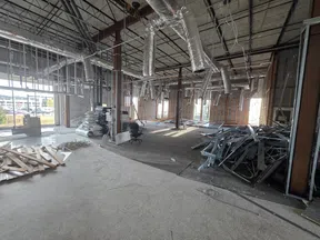 Interior view of a commercial space under construction with exposed ducts, metal studs, and construction materials scattered