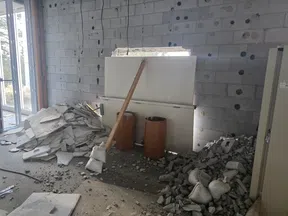 Construction site with broken concrete, rubble piles, sandbags, two barrels, and a wooden plank supporting a makeshift barrier.