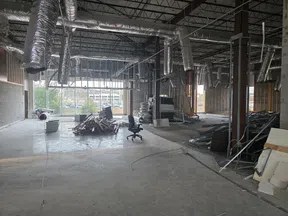 Interior of a large commercial space under construction with exposed ducts, materials, and office chairs inside.