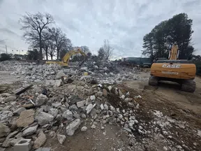 Construction site with excavators and rubble piles under a cloudy sky during demolition work.