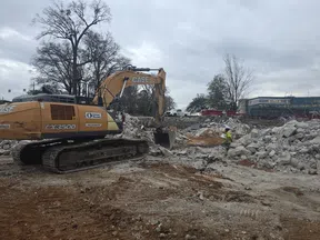 CASE excavator at a construction site clearing debris with a worker in safety gear and cloudy sky in background