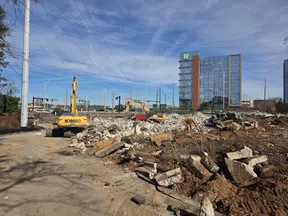 Construction site with excavators clearing rubble and debris near modern glass office buildings under a blue sky.