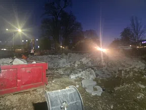 Construction site at night with rubble, excavators, and bright floodlights illuminating the area.