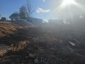 Sunny construction site with piles of gravel, dirt, and machinery under a clear blue sky with scattered clouds.