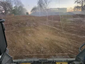 View through scratched dirty glass of construction vehicle overlooking a leveled dirt construction site at sunset.