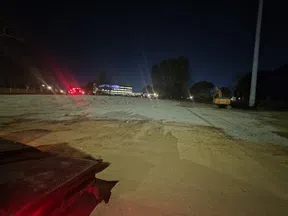 Night view of a construction site with gravel surface, excavator, and distant illuminated building under dark sky.
