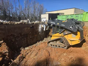 John Deere 325G compact track loader excavating a deep trench on a sunny day at a construction site.