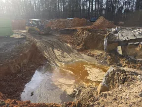 Construction site with muddy water, earth excavation, a bulldozer, and piles of dirt under sunlight.