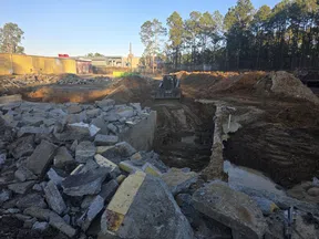 Construction site with broken concrete debris, excavated soil, and a bulldozer working under clear sky.