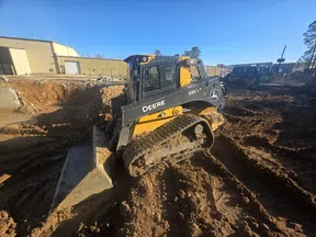 John Deere 335LP compact track loader working on muddy construction site under clear blue sky.