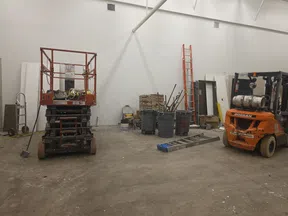 Construction equipment and tools including a scissor lift, forklift, ladders, and trash bins in an indoor workspace.
