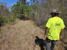 Man in bright yellow shirt and cap walking through a dry grassy path surrounded by trees on a clear sunny day