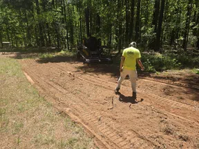Worker in bright shirt preparing soil with landscaping equipment in a sunlit forest clearing