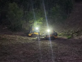 Two compact bulldozers with headlights on clearing forested land during night time.