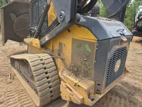 Close-up of a yellow tracked skid steer loader with dirt and leaves on it at a construction site.