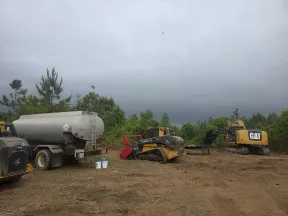 Construction site with Caterpillar excavator, John Deere skid steer loader, water tanker, and overcast sky