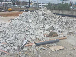 Large pile of concrete rubble and debris at an urban construction site near busy roads.